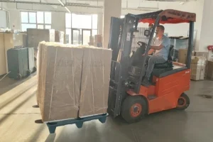 A worker on a forklift moving a large, packaged industrial commercial dehumidifier on a pallet in a warehouse.