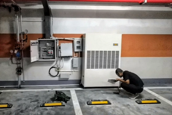 a worker inspects a large white commercial dehumidifier in a parking garage basement