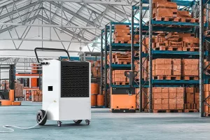 A mobile high temperature dehumidifier operating in an industrial warehouse, with pallets and boxes on high racks.